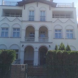 Lemberg Bud Sp. z o. o - Elewacja trzypiętrowego budynku z balkonami i tarasem na dachu, utrzymana w jasnej kolorystyce. Widoczne liczne okna z dekoracyjnymi elementami architektonicznymi.