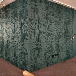 Lemberg Bud Sp. z o. o - Wykończone wnętrze z dekoracyjną, trójwymiarową ścianą w kolorze morskim, imitującą obwody drukowane. Widoczny fragment drzwi i podłogi.