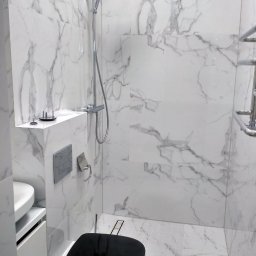 Lemberg Bud Sp. z o. o - Nowoczesna łazienka z kabiną prysznicową typu walk-in, wykończona białym marmurem, z czarną deską sedesową i chromowaną armaturą. Minimalistyczny design.