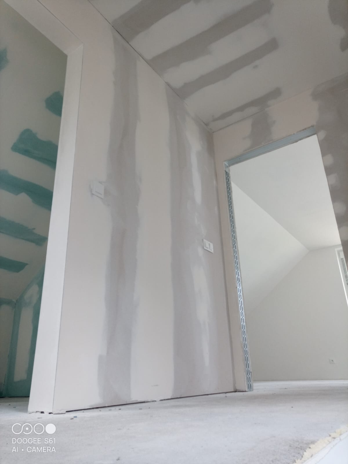 Wnętrze w trakcie prac wykończeniowych: ściany i sufit pokryte gładzią, widoczne profile przy otworach drzwiowych. Detal wykończenia wnętrza w surowym stanie.