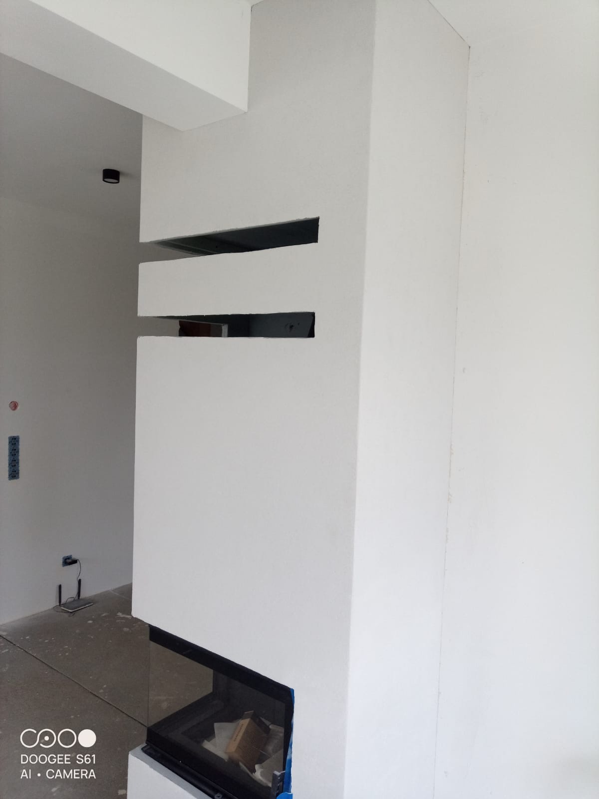 Biały, minimalistyczny kominek z poziomymi szczelinami w obudowie, widoczny fragment wnętrza z szarą podłogą i białymi ścianami. Nowoczesny design.