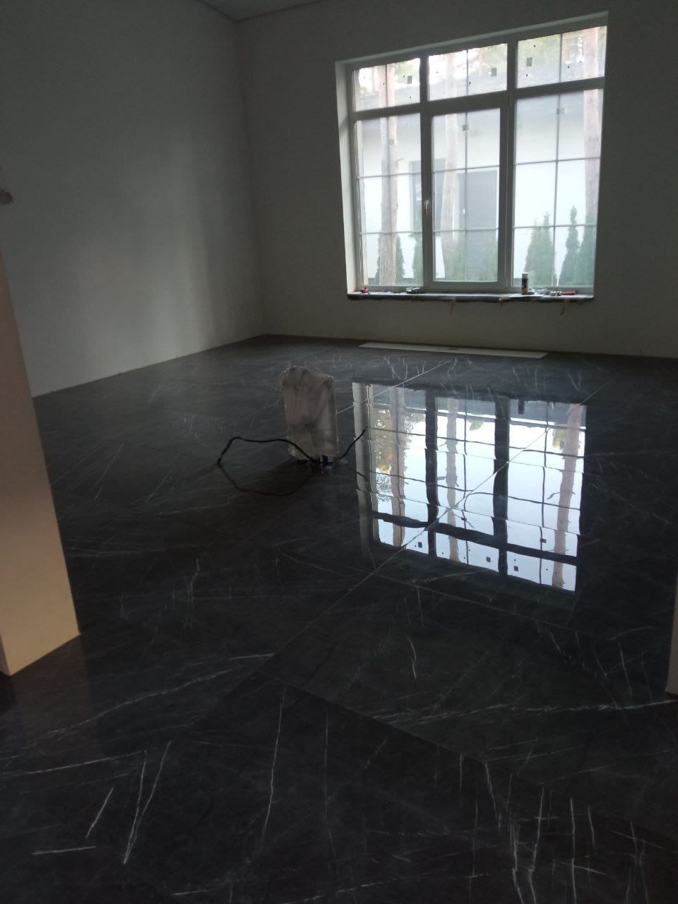 Błyszcząca, ciemna podłoga z płytek imitujących marmur w pustym pokoju. Widoczne duże okno z refleksami światła. Ujęcie z niskiego kąta, podkreślające połysk podłogi.