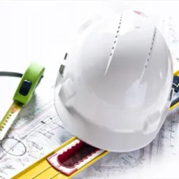 Biały kask budowlany, poziomica i zwinięta miarka na planach architektonicznych. Narzędzia pracy inżyniera na jasnym tle, detale projektu.