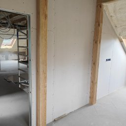SERWIS BUDOWLANY DOMINIK KOCIUBA - Montaż płyt gipsowo-kartonowych na drewnianej konstrukcji w poddaszu. Widoczne izolacje piankowe i elementy instalacji wentylacyjnej. Surowy stan wykończenia.