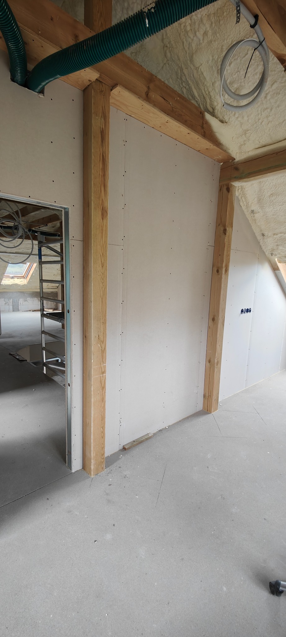 Montaż płyt gipsowo-kartonowych na drewnianej konstrukcji w poddaszu. Widoczne izolacje piankowe i elementy instalacji wentylacyjnej. Surowy stan wykończenia.