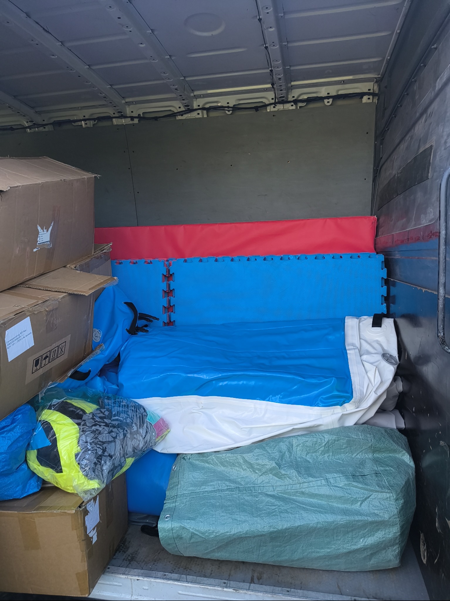 Wnętrze busa załadowane kartonami, matami i workami z wyposażeniem sportowym podczas transportu w Białystoku. Widok z tyłu pojazdu.