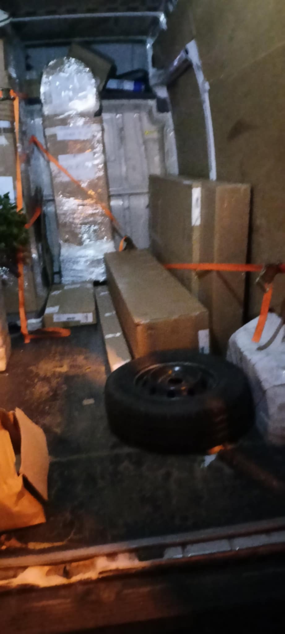 Wnętrze busa załadowane kartonami i zabezpieczone pasami transportowymi. Widoczne koło zapasowe. Nocne oświetlenie wnętrza pojazdu.