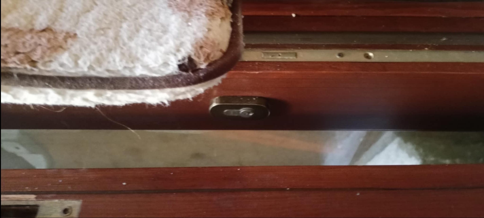 Fragment mebla z brązowego drewna z zamkiem i szufladą wyłożoną materiałem. Widoczne ślady użytkowania i drobne zabrudzenia.