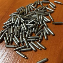 Minitech Adam Palma - Precyzyjnie wykonane, metalowe kołki o cylindrycznym kształcie z zaokrąglonymi końcami, ułożone na drewnianej powierzchni. Detal obróbki CNC lub tokarskiej.