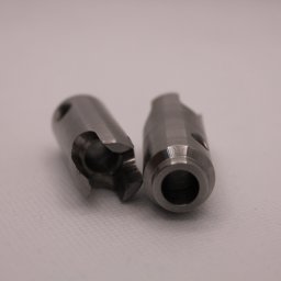 Minitech Adam Palma - Dwa metalowe, cylindryczne elementy z precyzyjnymi wycięciami i otworami, leżące obok siebie na jasnym tle. Widoczne ślady obróbki.