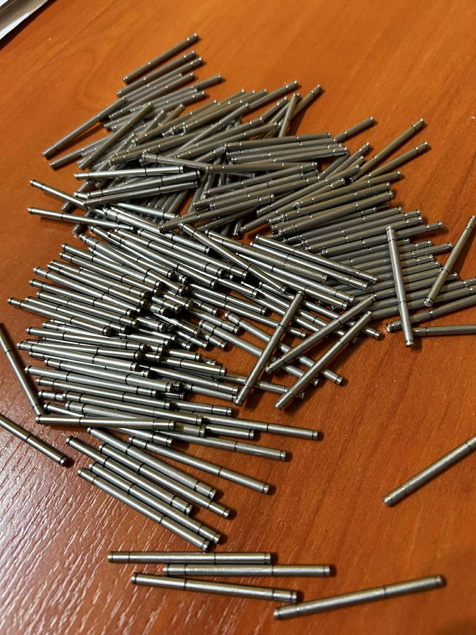 Partia metalowych, cylindrycznych elementów z rowkiem na drewnianym blacie. Detale wykonane z precyzją, prawdopodobnie po obróbce.