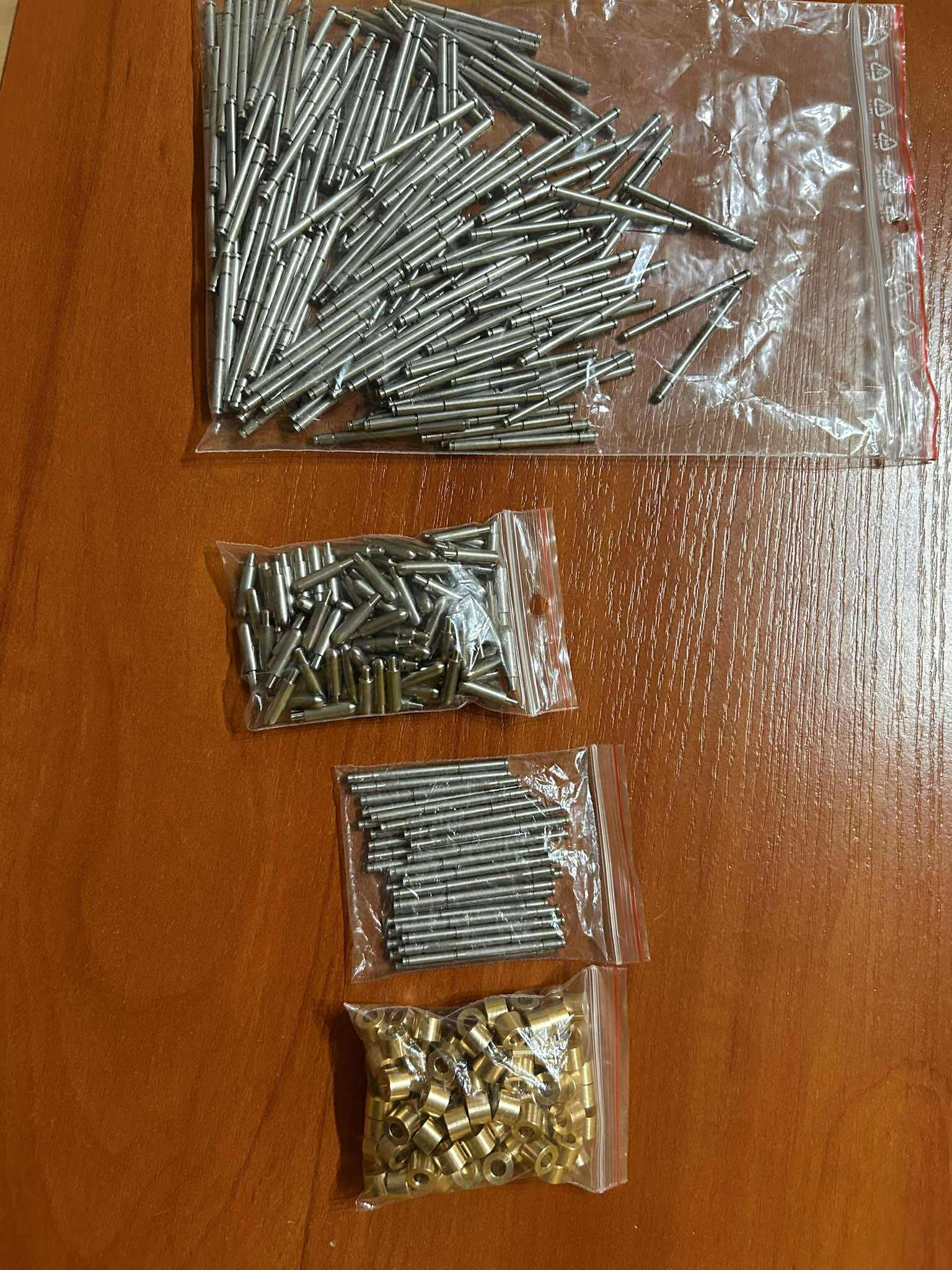 Metalowe elementy w przezroczystych woreczkach strunowych na drewnianej powierzchni. Różne kształty i kolory, prawdopodobnie detale po obróbce.