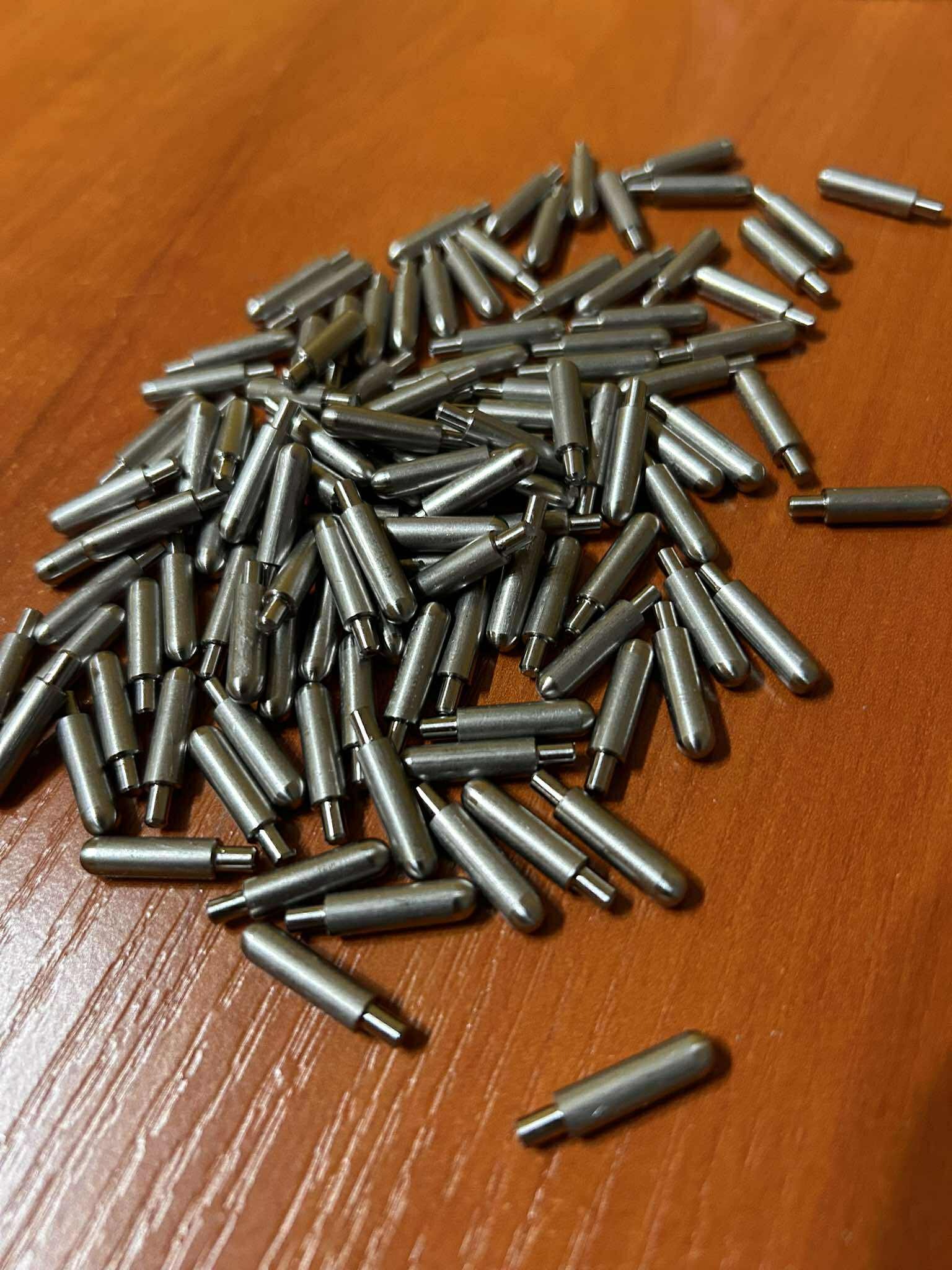 Precyzyjnie wykonane, metalowe kołki o cylindrycznym kształcie z zaokrąglonymi końcami, ułożone na drewnianej powierzchni. Detal obróbki CNC lub tokarskiej.