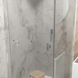 Nowoczesna kabina prysznicowa z marmurowymi płytkami, deszczownicą i drewnianym stołkiem. Minimalistyczny design, szklane ściany, jasne wnętrze.