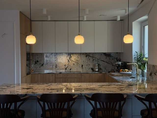 Nowoczesna kuchnia z wyspą: drewniane szafki dolne, białe górne, marmurowy blat i backsplash. Trzy wiszące lampy z mlecznego szkła.