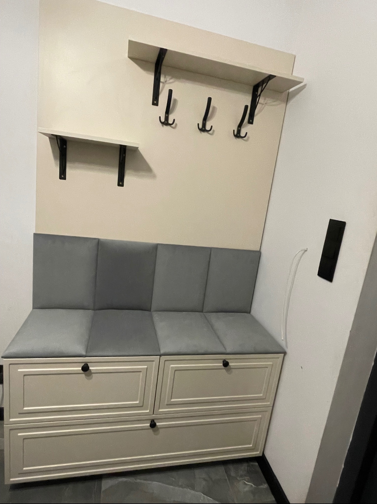 Funkcjonalna zabudowa przedpokoju: siedzisko z szufladami, półka i wieszaki na ścianie w jasnej tonacji. Nowoczesny design z elementami klasycznymi.