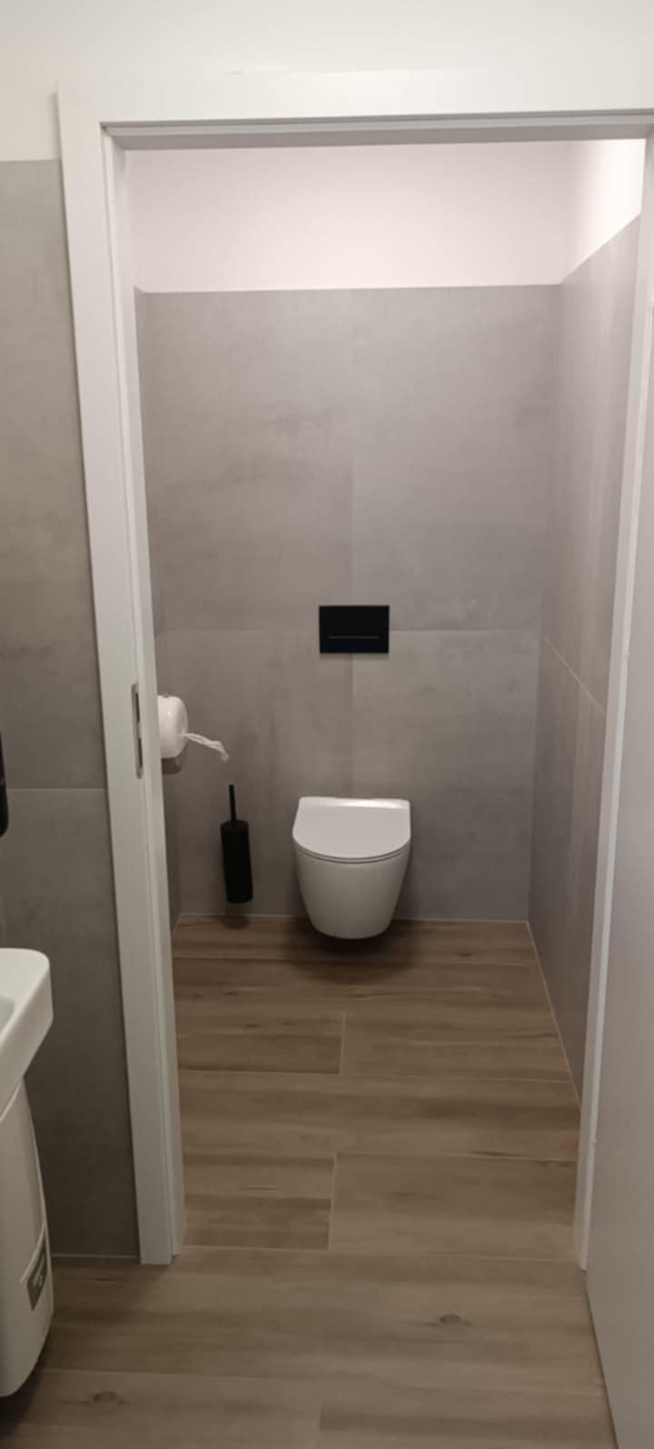 Wykończona łazienka w Warszawie z drewnopodobną podłogą i szarymi płytkami ściennymi. Wisząca toaleta i minimalistyczny design.