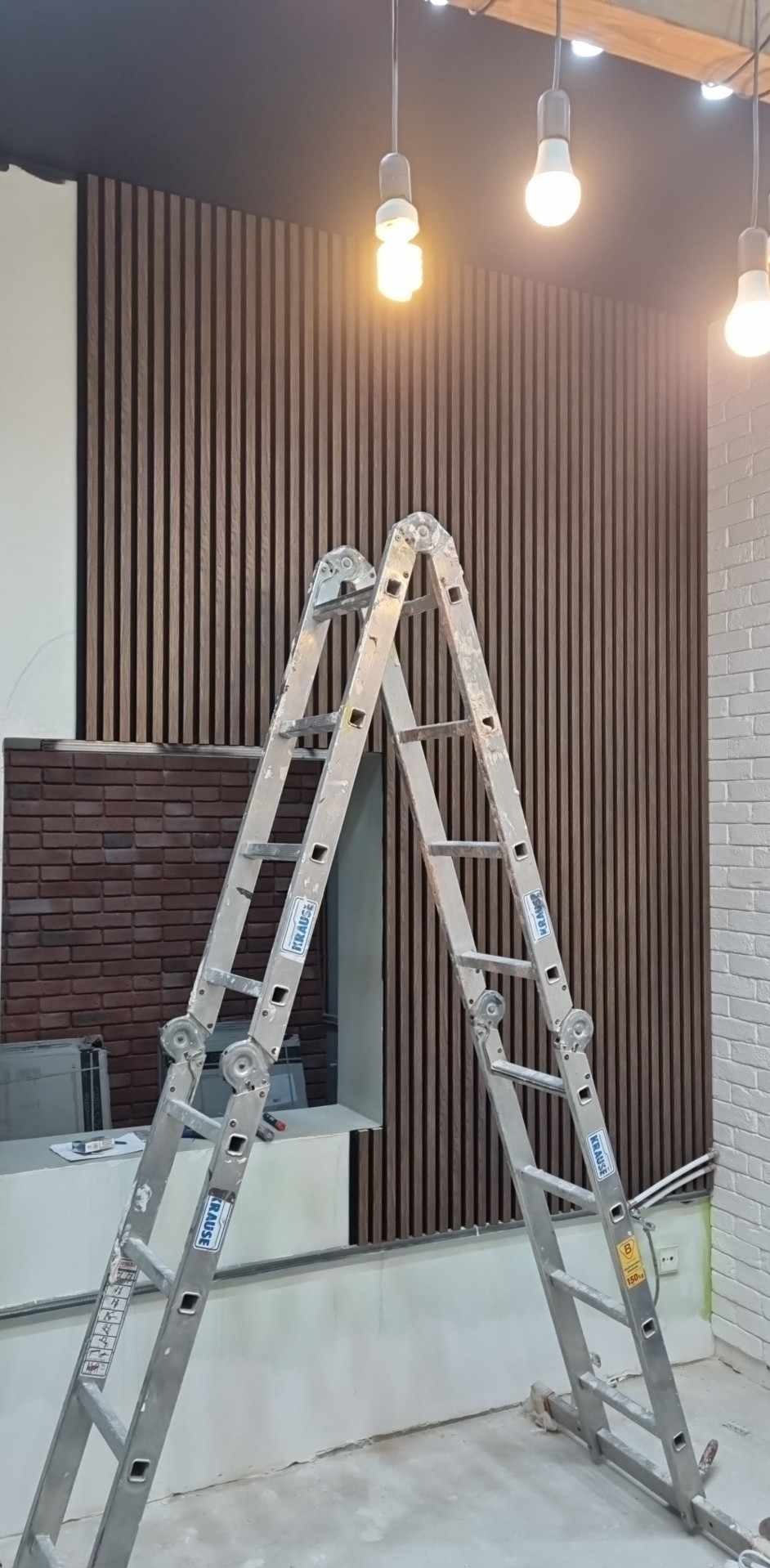 Wykończenie wnętrza: drewniane lamele pionowe na ścianie, fragment ściany z cegły i drabina Krause. Oświetlenie sufitowe.