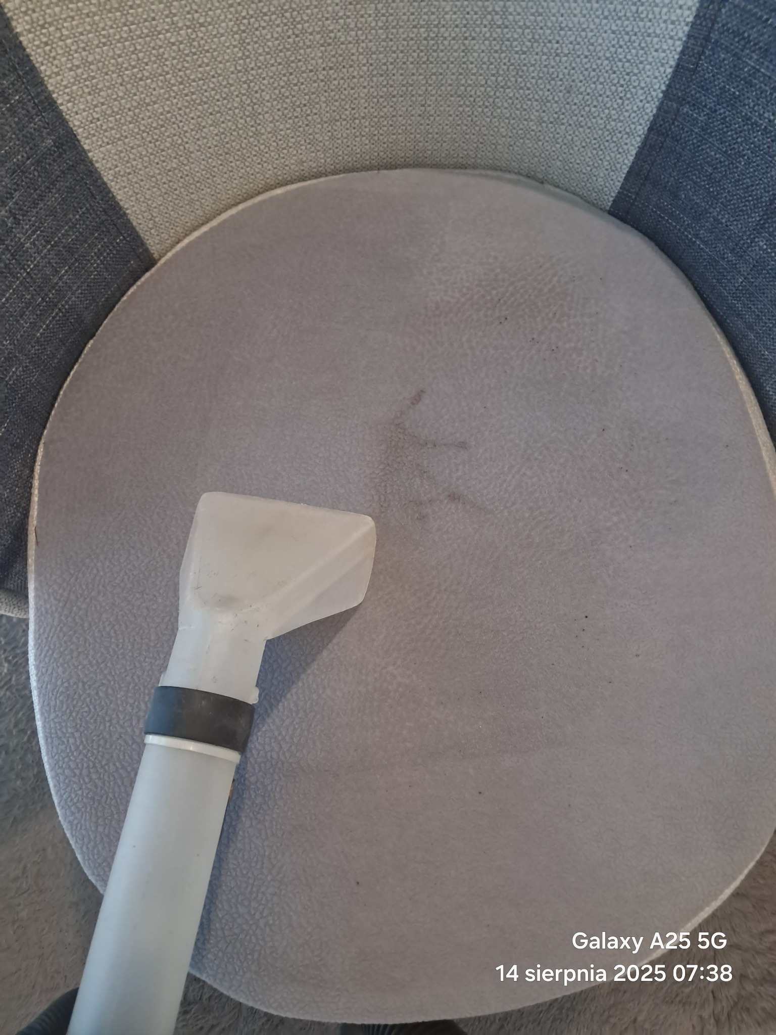 Dysza odkurzacza piorącego na szarym, okrągłym siedzisku krzesła. Widoczne ślady po plamach. Ujęcie z góry, bliskie. Data i model telefonu w prawym dolnym rogu.