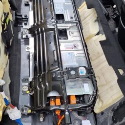 AutoKlinika Dominik Budzelewski - Wnętrze samochodu z widoczną baterią trakcyjną w trakcie montażu lub demontażu, z odsłoniętymi przewodami i elementami instalacji elektrycznej.