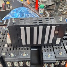 AutoKlinika Dominik Budzelewski - Otwarta bateria samochodu elektrycznego z widocznymi modułami i śrubami mocującymi, na roboczym stole warsztatu.