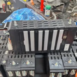 Otwarta bateria samochodu elektrycznego z widocznymi modułami i śrubami mocującymi, na roboczym stole warsztatu.