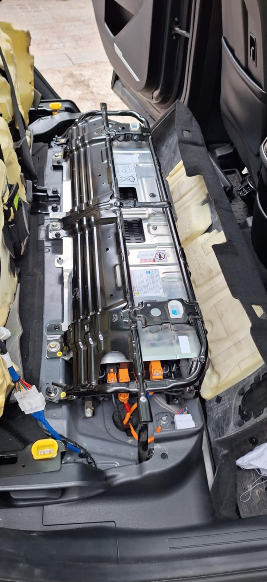 Wnętrze samochodu z widoczną baterią trakcyjną w trakcie montażu lub demontażu, z odsłoniętymi przewodami i elementami instalacji elektrycznej.