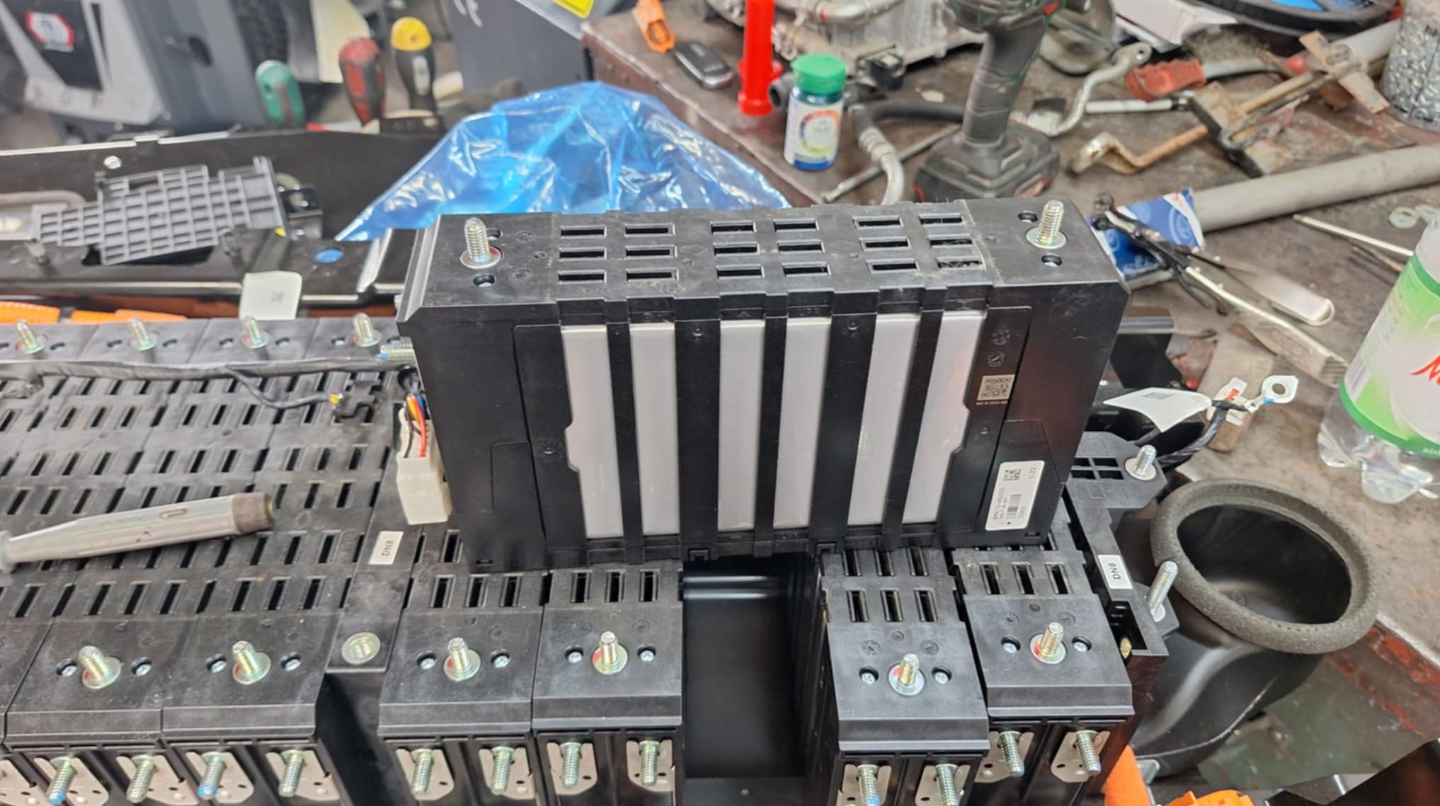 Otwarta bateria samochodu elektrycznego z widocznymi modułami i śrubami mocującymi, na roboczym stole warsztatu.