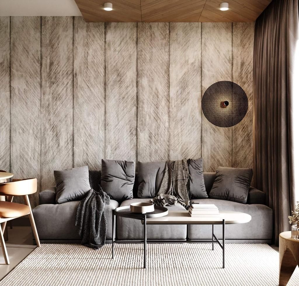 Stylowy salon z szarą sofą, teksturowaną ścianą i okrągłą lampą. Neutralna kolorystyka i minimalistyczny design. Widoczny stolik kawowy i dywan w jasnym odcieniu.