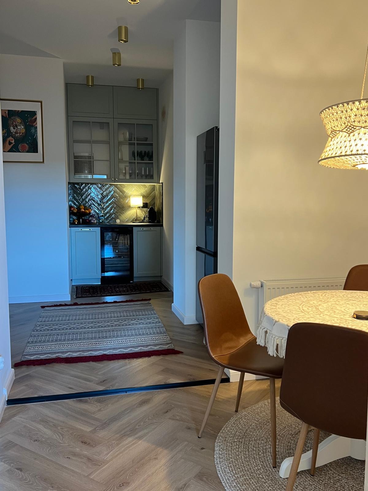 Stylowa aranżacja wnętrza: parkiet w jodełkę, dywan z wzorem etnicznym i zabudowa kuchenna w odcieniach szarości z dekoracyjną mozaiką na ścianie.