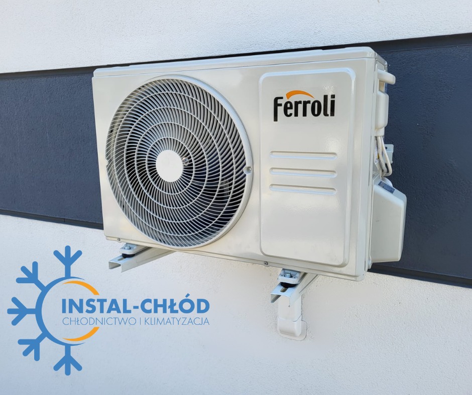 Klimatyzator Ferroli zamontowany na białej elewacji budynku w Łabiszynie. Widoczne mocowania i fragment logo firmy Instal-Chłód na dole zdjęcia.
