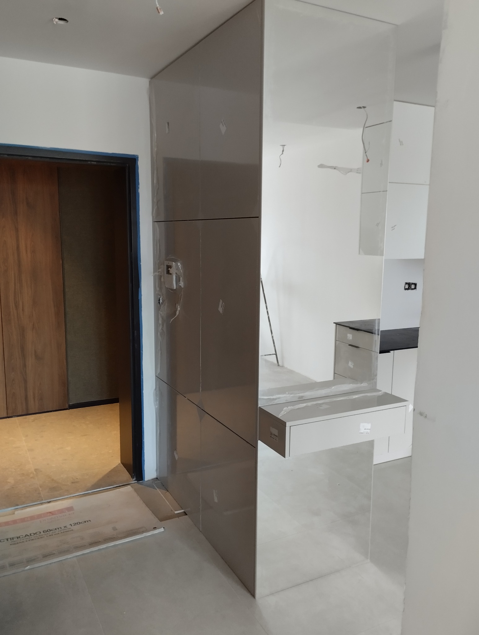 Montaż szafy z lustrzanymi frontami w przedpokoju; widoczne zabezpieczenia folią. W tle fragment kuchni i drzwi do pokoju. Nowoczesne wykończenie wnętrza.