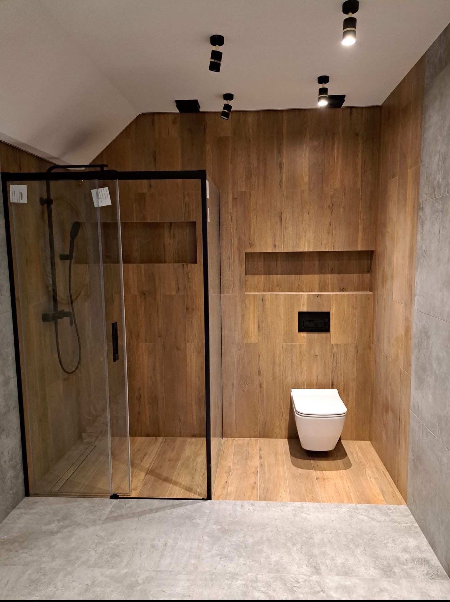 Nowoczesna łazienka z kabiną prysznicową typu walk-in, drewnopodobnymi płytkami na ścianach i podłodze, oraz podwieszaną miską WC. Oświetlenie punktowe.