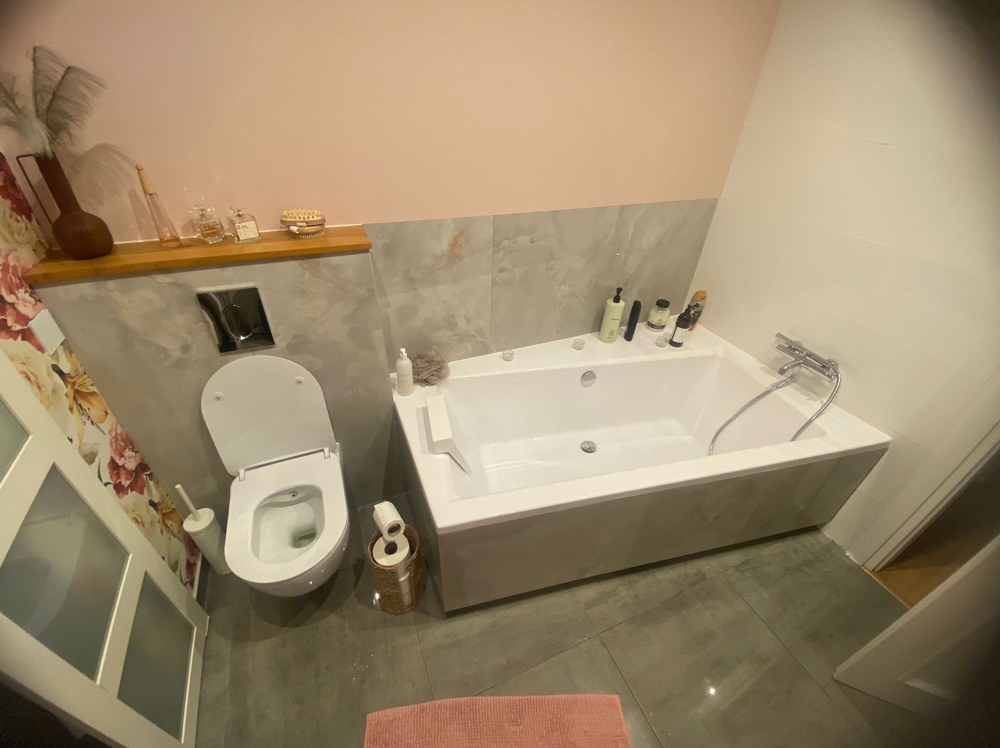 Jasna łazienka z wanną, toaletą i szarą glazurą. Nad toaletą półka z dekoracjami. Widok z góry na wykończone wnętrze łazienki.