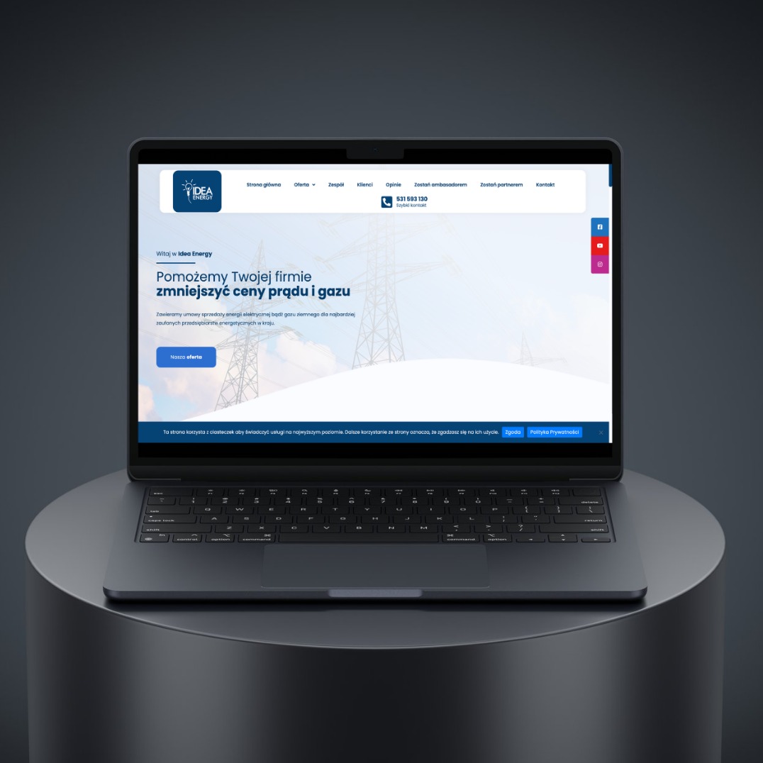 Laptop prezentuje stronę Idea Energy z hasłem 'Pomożemy Twojej firmie zmniejszyć ceny prądu i gazu'. Widoczne menu strony, logo i dane kontaktowe. Minimalistyczny design.