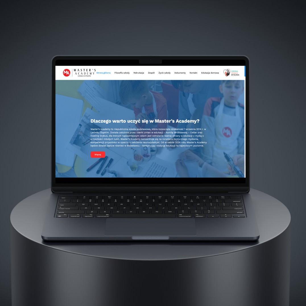 Laptop prezentuje stronę internetową Master's Academy z tekstem 'Dlaczego warto uczyć się w Master's Academy?' i zdjęciem dzieci w tle, na ciemnym, okrągłym postumencie.