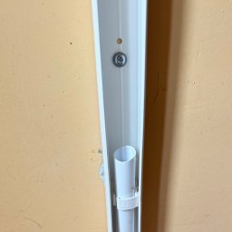 VeliWgroup - Zamocowana biała rura w korytku przy ścianie. Widoczny fragment ściany w kolorze beżowym oraz śruba mocująca koryto. Instalacja w trakcie montażu.