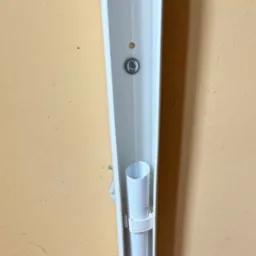 Zamocowana biała rura w korytku przy ścianie. Widoczny fragment ściany w kolorze beżowym oraz śruba mocująca koryto. Instalacja w trakcie montażu.