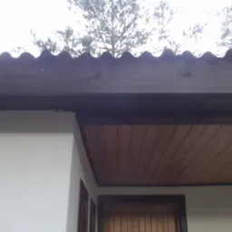 Fragment dachu z brązową falistą blachą, drewnianą podbitką i białą ścianą budynku, widok z dołu.