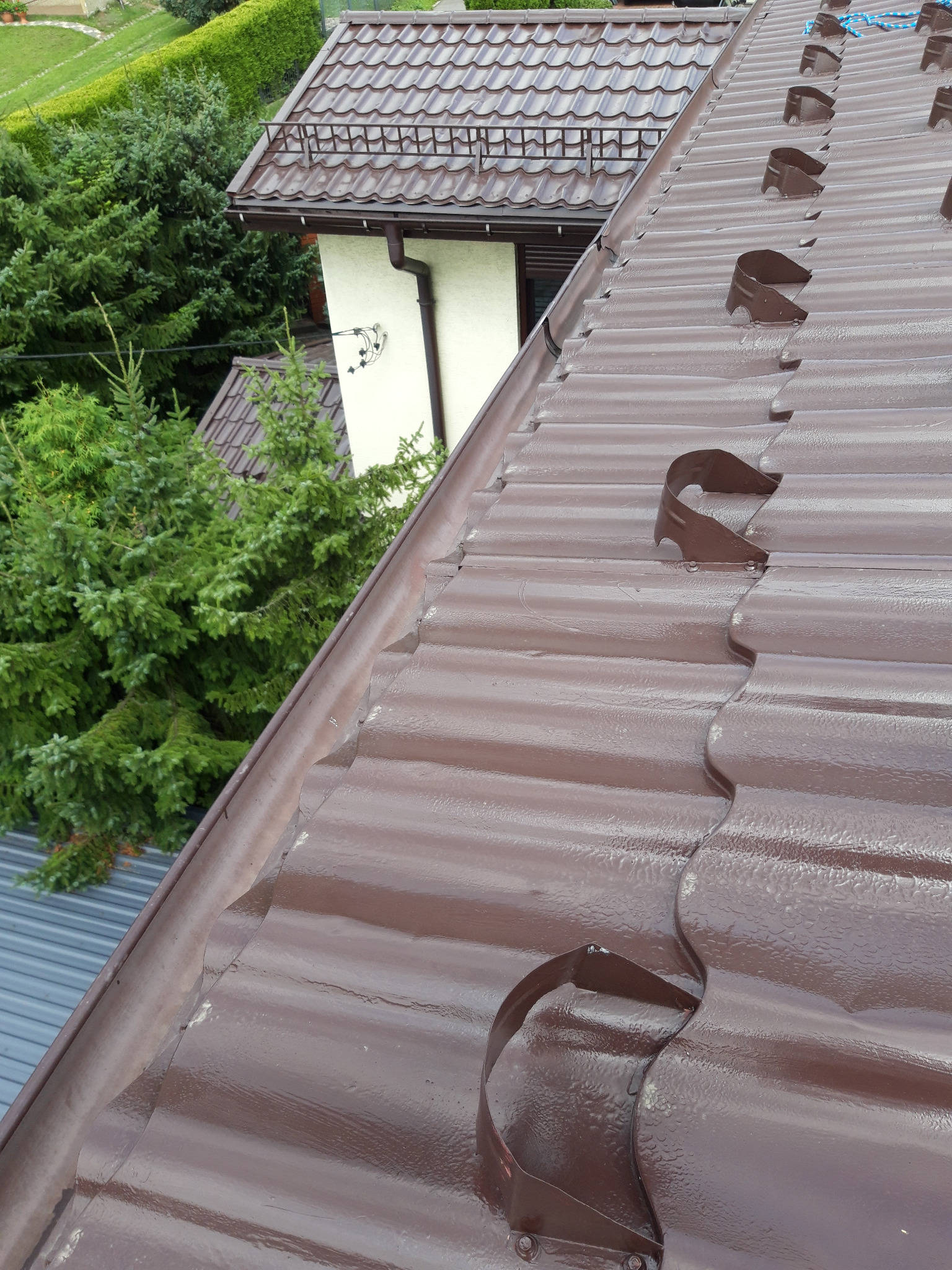 Brązowy, błyszczący dach z blachy trapezowej z zamontowanymi hakami do rynien, widok z góry.