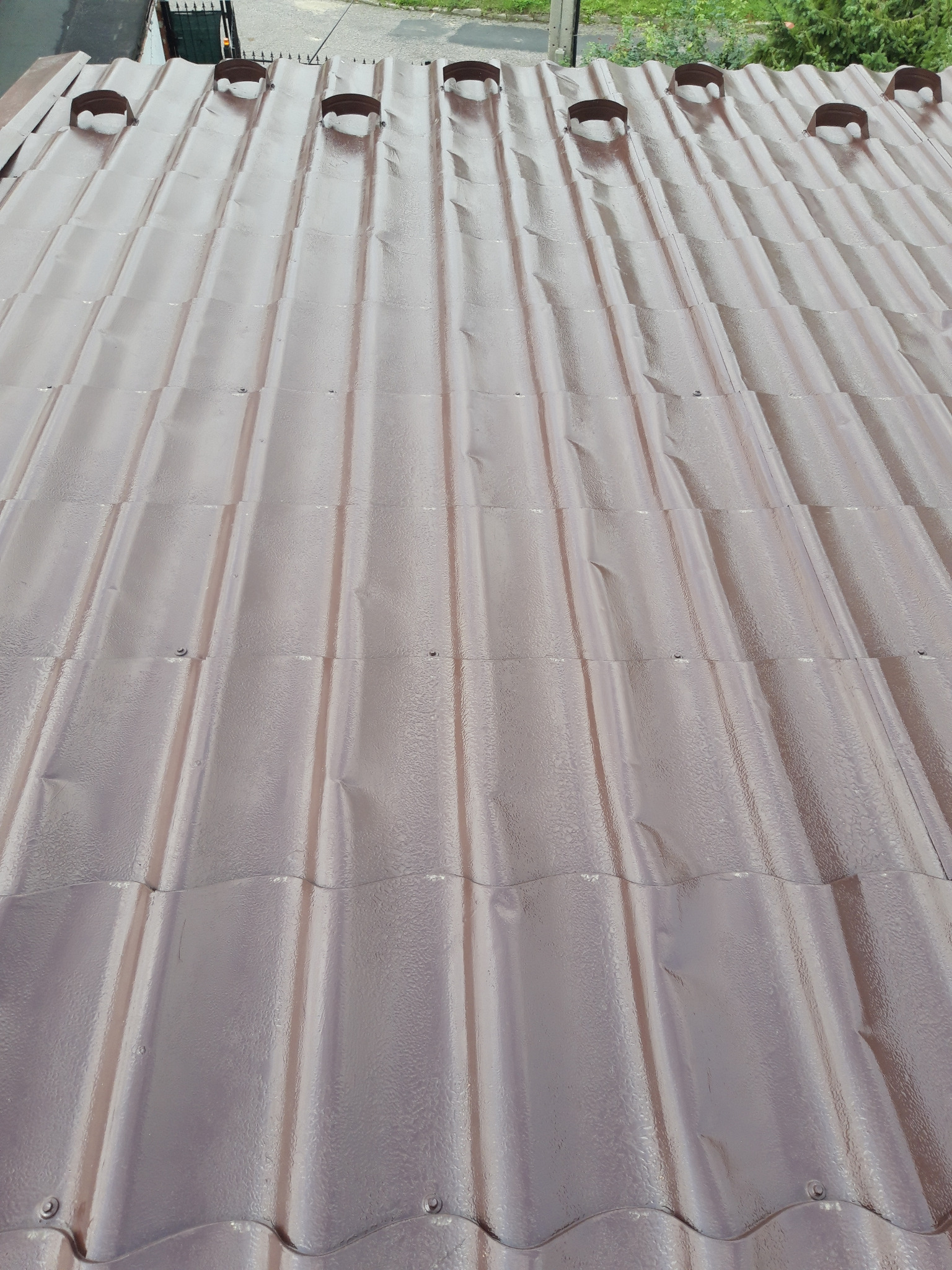 Metalowa dachówka w kolorze brązowym, widok z góry, z widocznymi mocowaniami i elementami wentylacyjnymi w górnej części dachu.