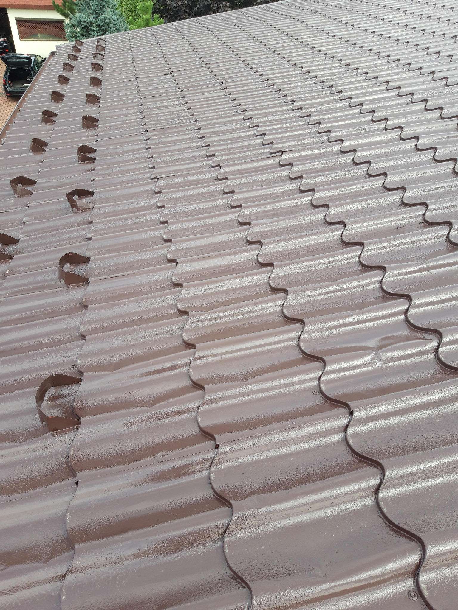 Brązowy dach z blachy trapezowej z zamontowanymi hakami do rynien w regularnych odstępach, widok z góry.