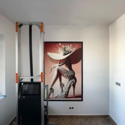 Wallplex - Drukarka pionowa maluje na ścianie obraz kobiety w kapeluszu. Parkiet na podłodze. Nowoczesne wykończenie wnętrza. Druk UV na ścianie.