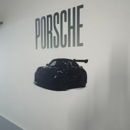 Wallplex - Grafika na ścianie przedstawia czarny samochód Porsche GT3 RS z napisem 'PORSCHE' powyżej, w minimalistycznym, nowoczesnym stylu.