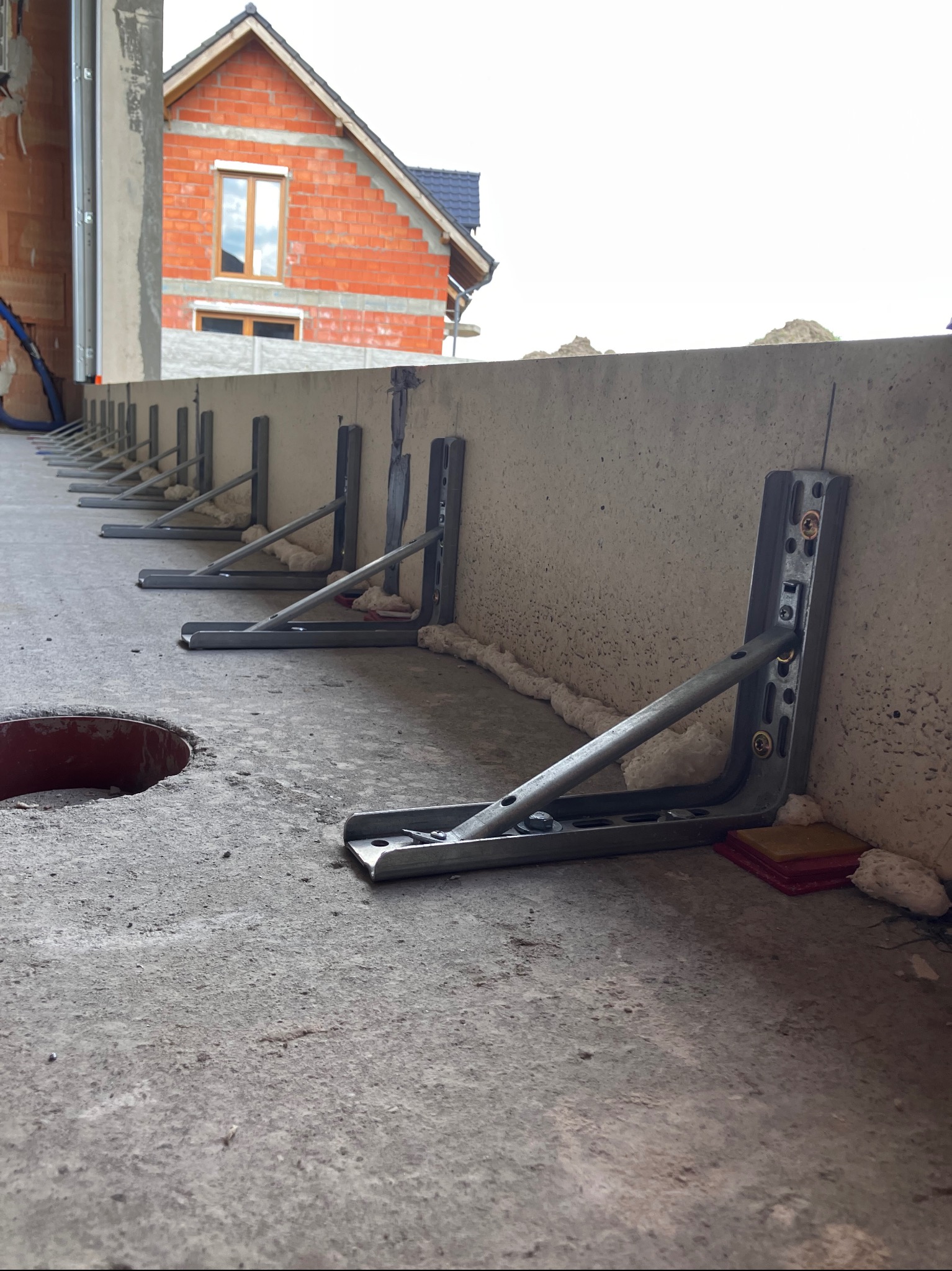 Metalowe wsporniki zamontowane na betonowym fundamencie, przygotowane do dalszych prac budowlanych, z widocznym budynkiem w tle.