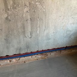Szymon Kopka - Instalacja rur (czerwona i niebieska) przy podłodze, wzdłuż surowej ściany, prawdopodobnie ogrzewanie podłogowe, instalacja wykonana przed zalaniem posadzki.