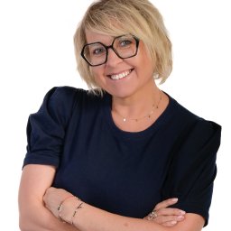 Tamka Foto Studio - Uśmiechnięta blond kobieta w okularach i granatowej koszulce, z założonymi rękami na białym tle. Portret.