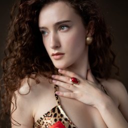 Tamka Foto Studio - Portret kobiety o kręconych włosach, z delikatnym makijażem, w bluzce z wzorem panterki i czerwonym pierścionkiem, pozującej na ciemnym tle.