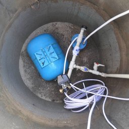 Wnętrze betonowej studni kręgowej z niebieskim zbiornikiem hydroforowym i instalacją wodną. Usługi studniarskie w Warszawie.