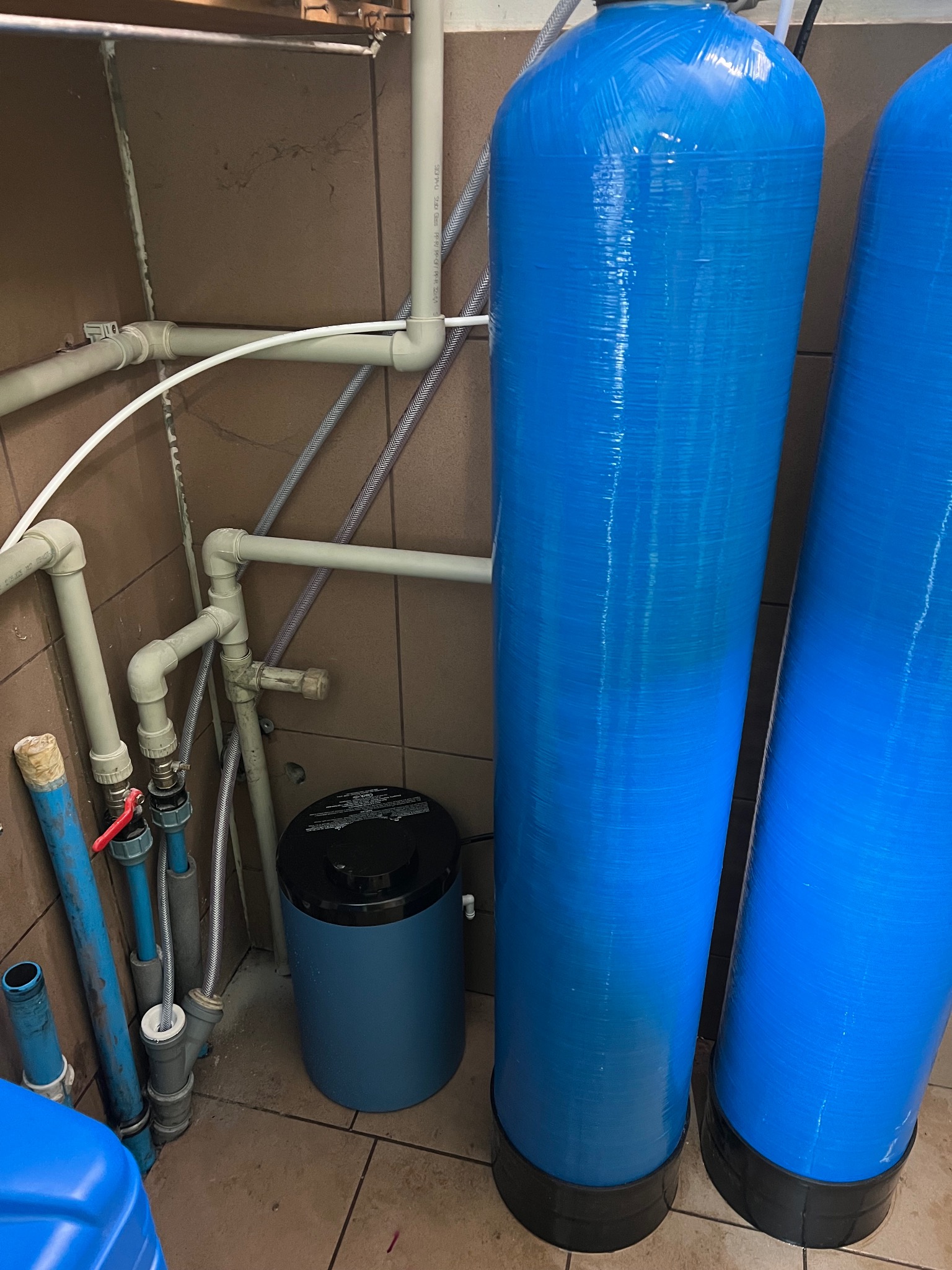 Niebieskie filtry do wody z rurami i zaworami w pomieszczeniu. Dwa duże cylindryczne filtry i mniejszy zbiornik obok instalacji wodnej.